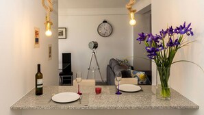 Uma cozinha moderna com uma ilha central, dois banquetes, uma garrafa de vinho e um vaso de flores.
