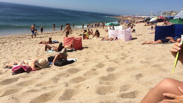 Uma praia cheia de gente tomando sol e passeando pela areia.