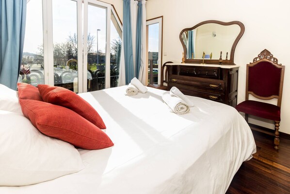 A hotel room with a large bed, a wooden dresser, a mirror, and a view of the outdoors. - Guest H4U Villa Garden Pool (Povoa De Varzim)