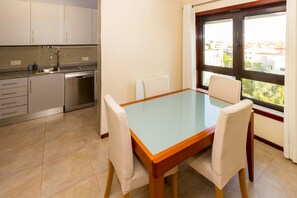Una pequeña cocina con lavavajillas, una ventana con cortinas y una mesa de comedor con sillas.