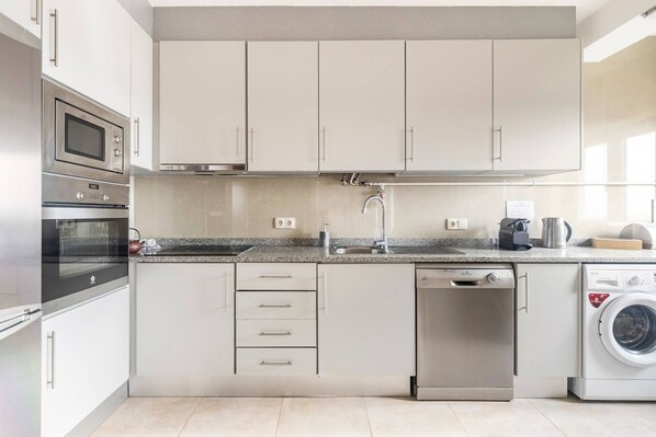 Una cocina moderna con electrodomésticos de acero inoxidable, encimera de granito y armarios blancos.