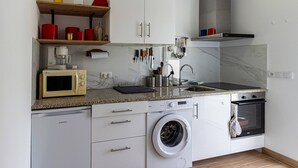 Uma cozinha compacta com máquina de lavar, micro-ondas, forno e pia, equipada com diversos utensílios.