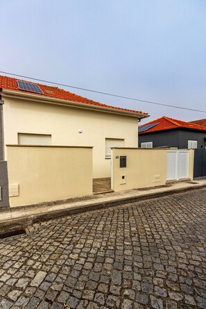 A building with a beige facade, a red-tiled roof, and a cobblestone street. - Guest H4U - Jard n y Playa Mindelo (Vila do Conde)