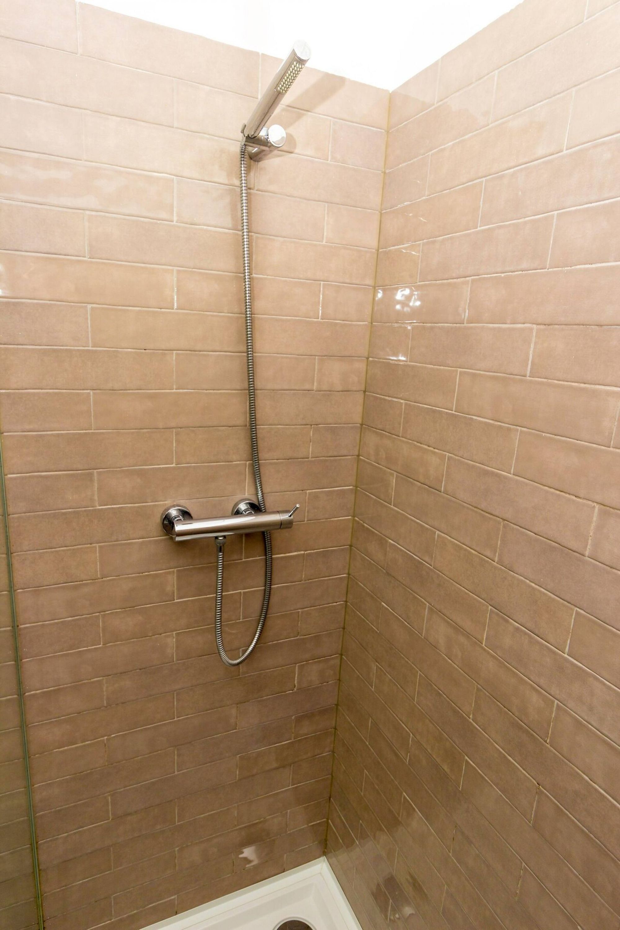 A shower with a handheld showerhead and a wall-mounted faucet.