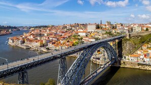 Un gran puente de acero que cruza un río sobre una ciudad histórica con edificios de techo rojo y una iglesia destacada.