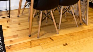 Un comedor con una mesa blanca y cuatro sillas negras, un separador de madera con motivos de hojas, y dos cuadros en la pared.