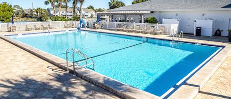 A rectangular swimming pool with clear blue water, surrounded by a tiled deck and lounge chairs.