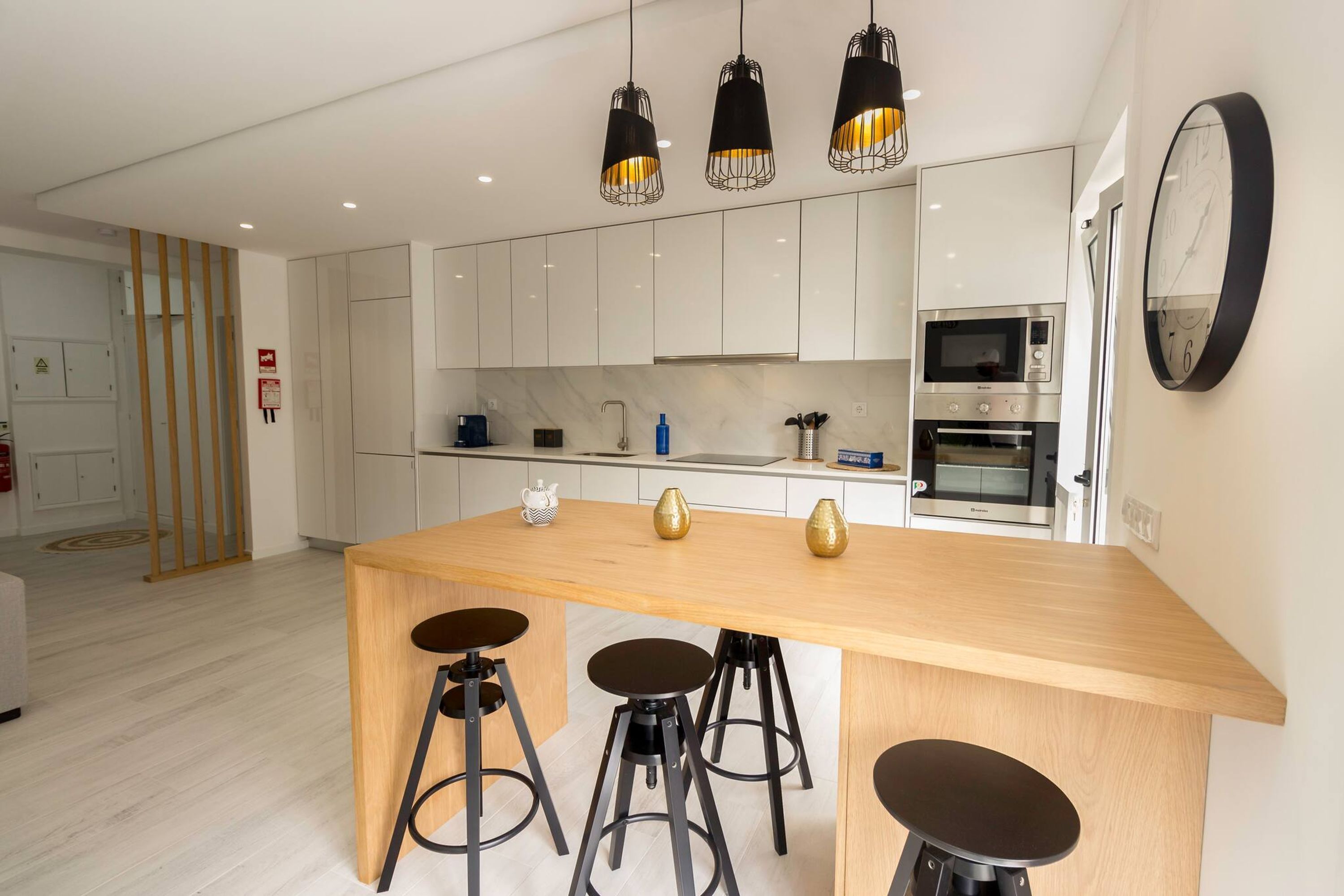 A modern kitchen with white cabinets, a wooden island with stools, and pendant lighting.