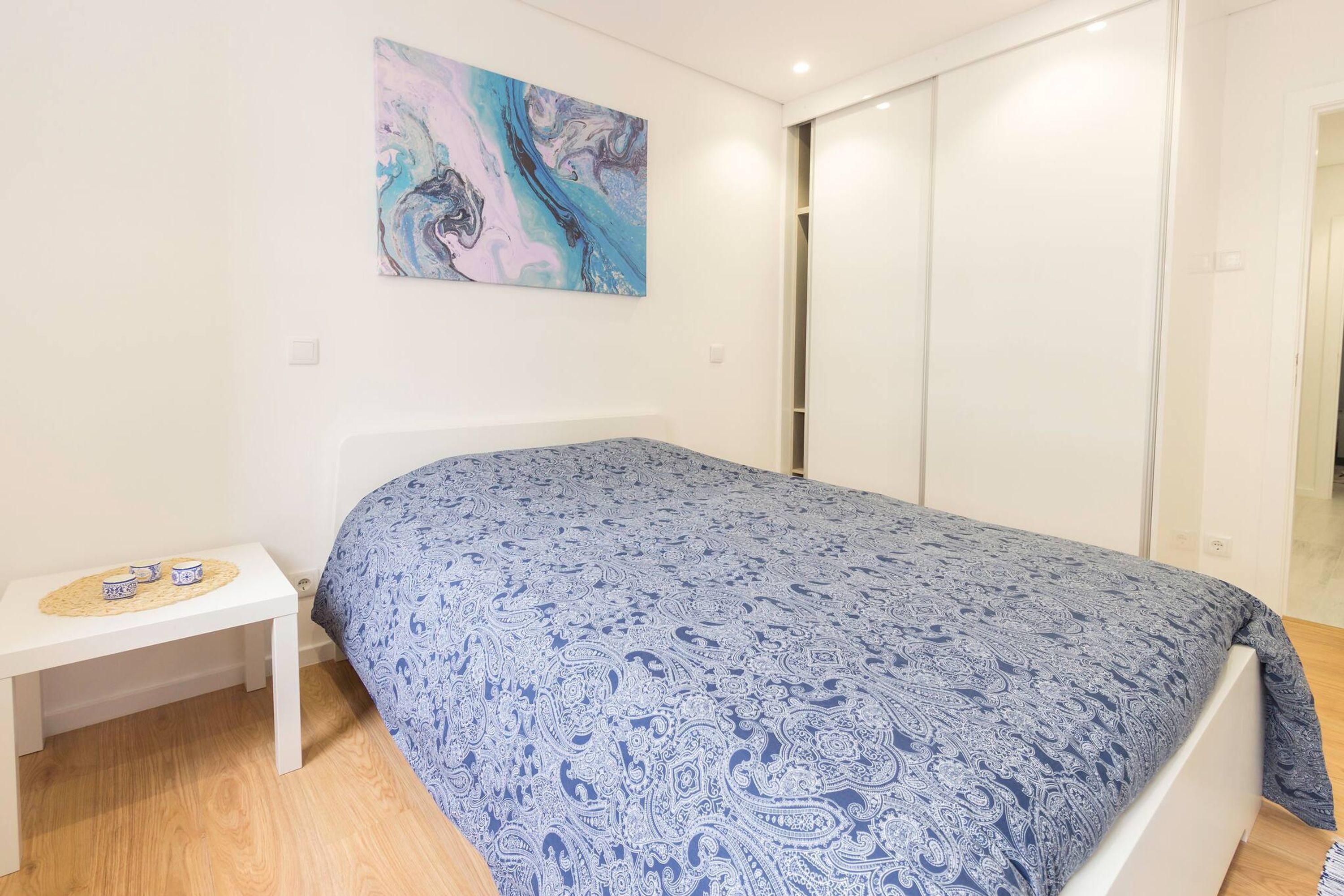 Ein Schlafzimmer mit Bett, Nachttisch, einem an der Wand hängenden abstrakten Gemälde und einem Kleiderschrank.