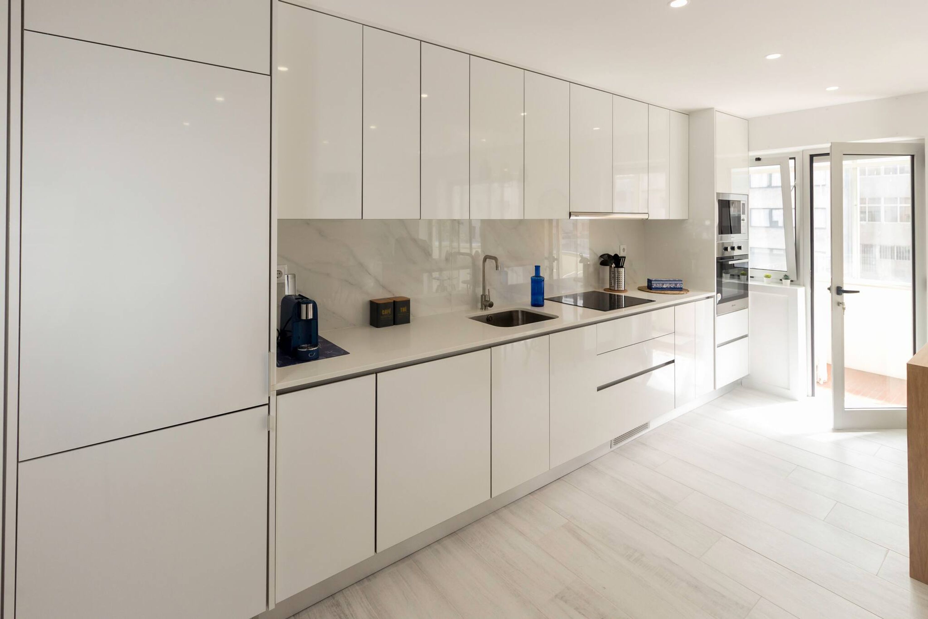 Una cocina moderna con armarios blancos, salpicadero de mármol y electrodomésticos de acero inoxidable.
