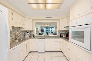 A modern kitchen with white cabinetry, a granite countertop, and a built-in oven. - Shoreline Towers 1055 2 Bedroom Condo (Destin)
