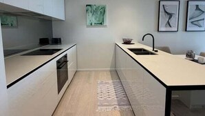 Moderni keittiö, jossa on valkoiset kaapit, keskellä oleva saareke ja ruokailutila.