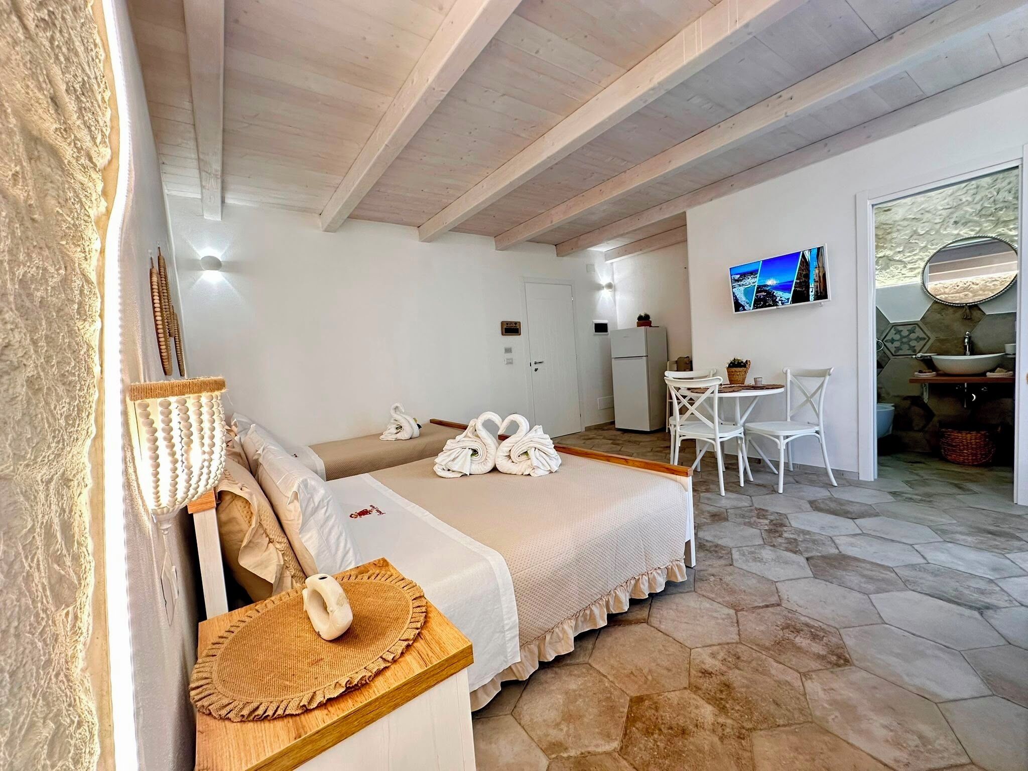 A bedroom with a bed, a sitting area with a table and chairs, a television, and a bathroom with a sink and mirror.