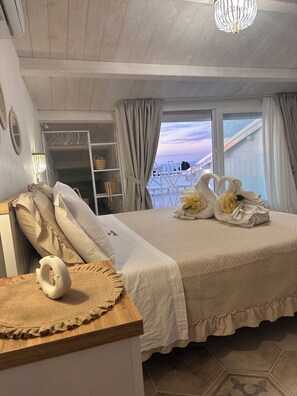A hotel room with a bed, a wooden dresser, a mirror, a hanging light fixture, and a window with a view. - Godano Rooms (Drapia)