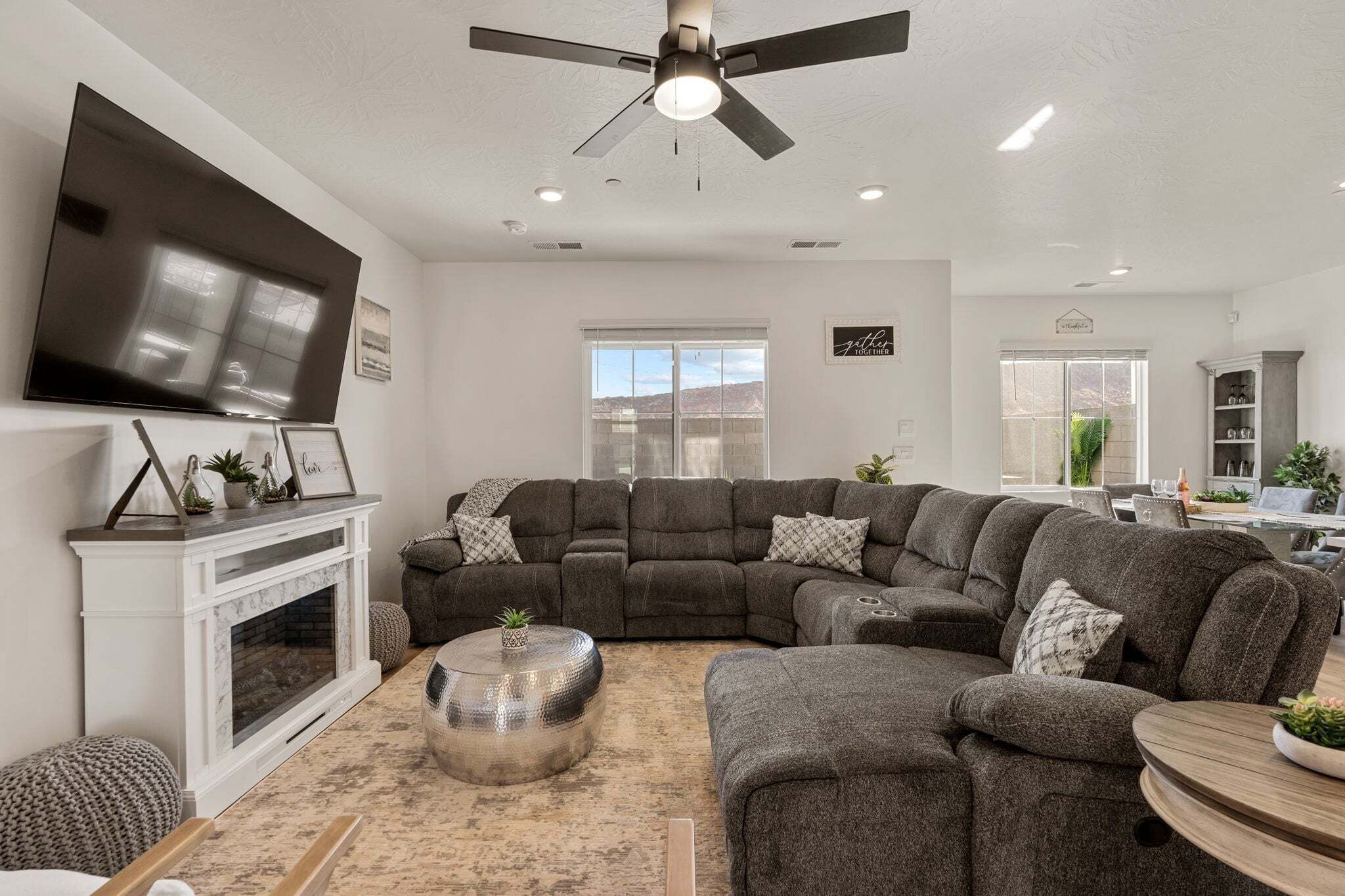 Un salon moderne avec un canapé d’angle, une cheminée, un téléviseur à écran plat et un ventilateur de plafond.