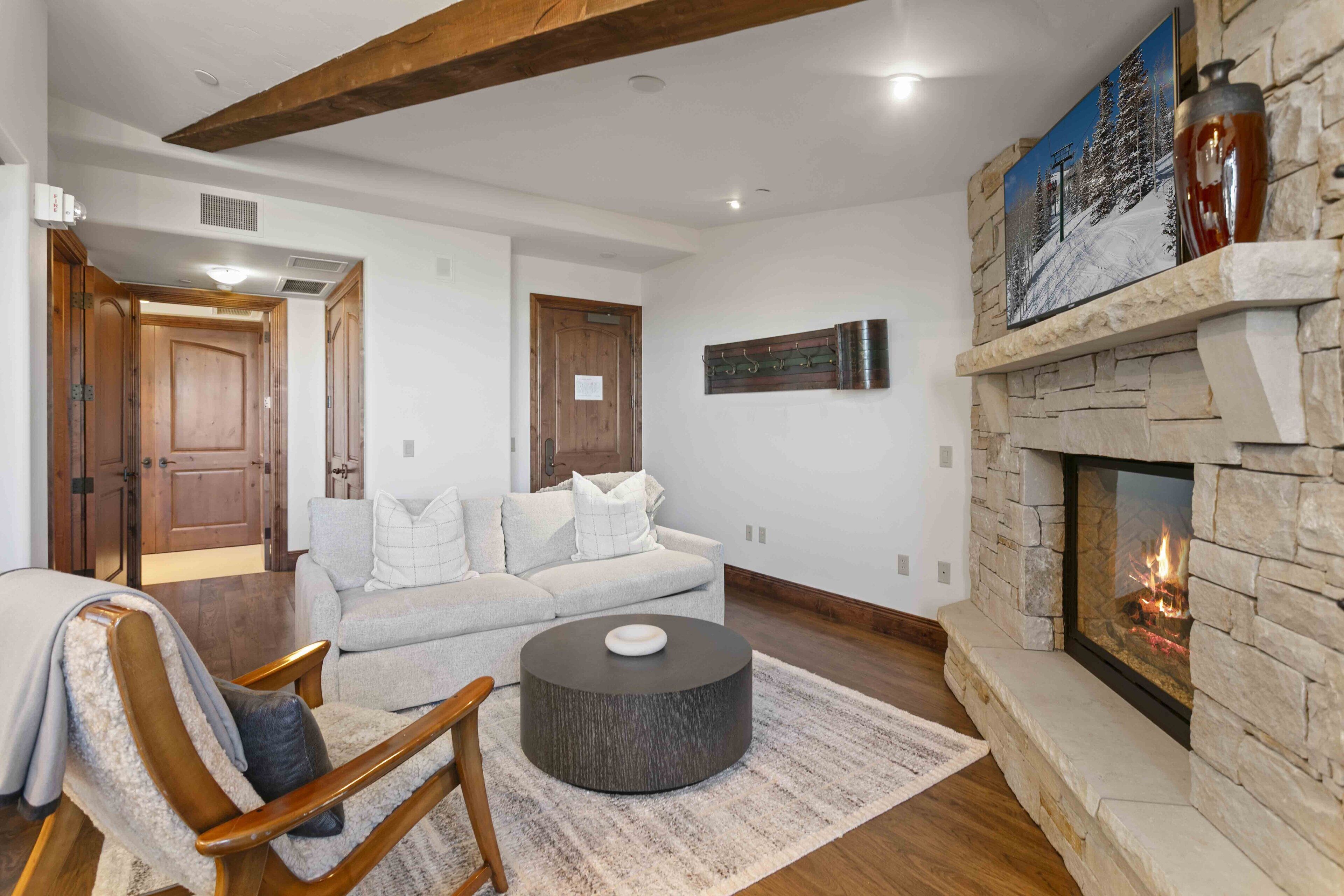 A living room with a stone fireplace, a grey sofa, a wooden coffee table, and a wooden chair.