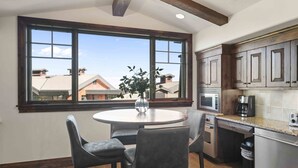 A kitchen with a large window, a round table with chairs, and modern appliances.