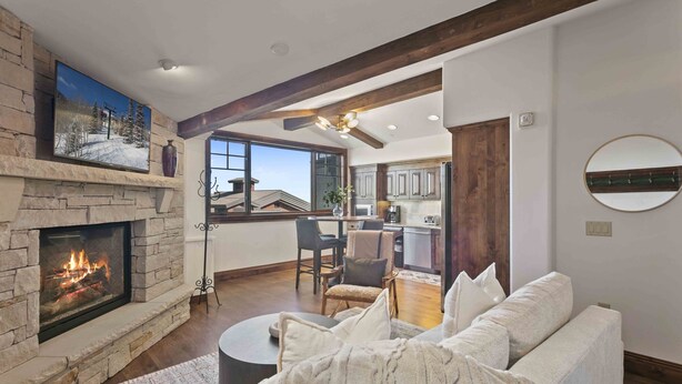 A living room with a stone fireplace, a white sofa, and a view of the kitchen and dining area.