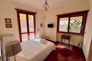 Ein Schlafzimmer mit einem großen Bett, einem Nachttisch, einer Lampe, einem an der Wand montierten Fernseher und einem Fenster mit Blick nach draußen.