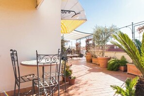 Un patio con una mesa redonda y sillas, plantas en macetas y un paraguas amarillo.