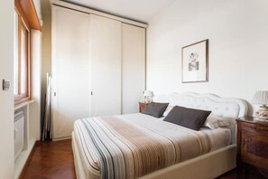 Un dormitorio con cama, armario, mesita de noche y un cuadro en la pared.