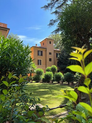 A building with a symmetrical facade, a central tower, and a well-maintained garden with various shrubs and a lawn. - Rome Epirus Suite - Your authentic retreat just minutes from the Colosseum (Roma)