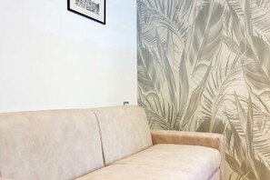 Ein beiges Sofa vor einer Wand mit großem Wandpapier mit tropischem Blattmuster.