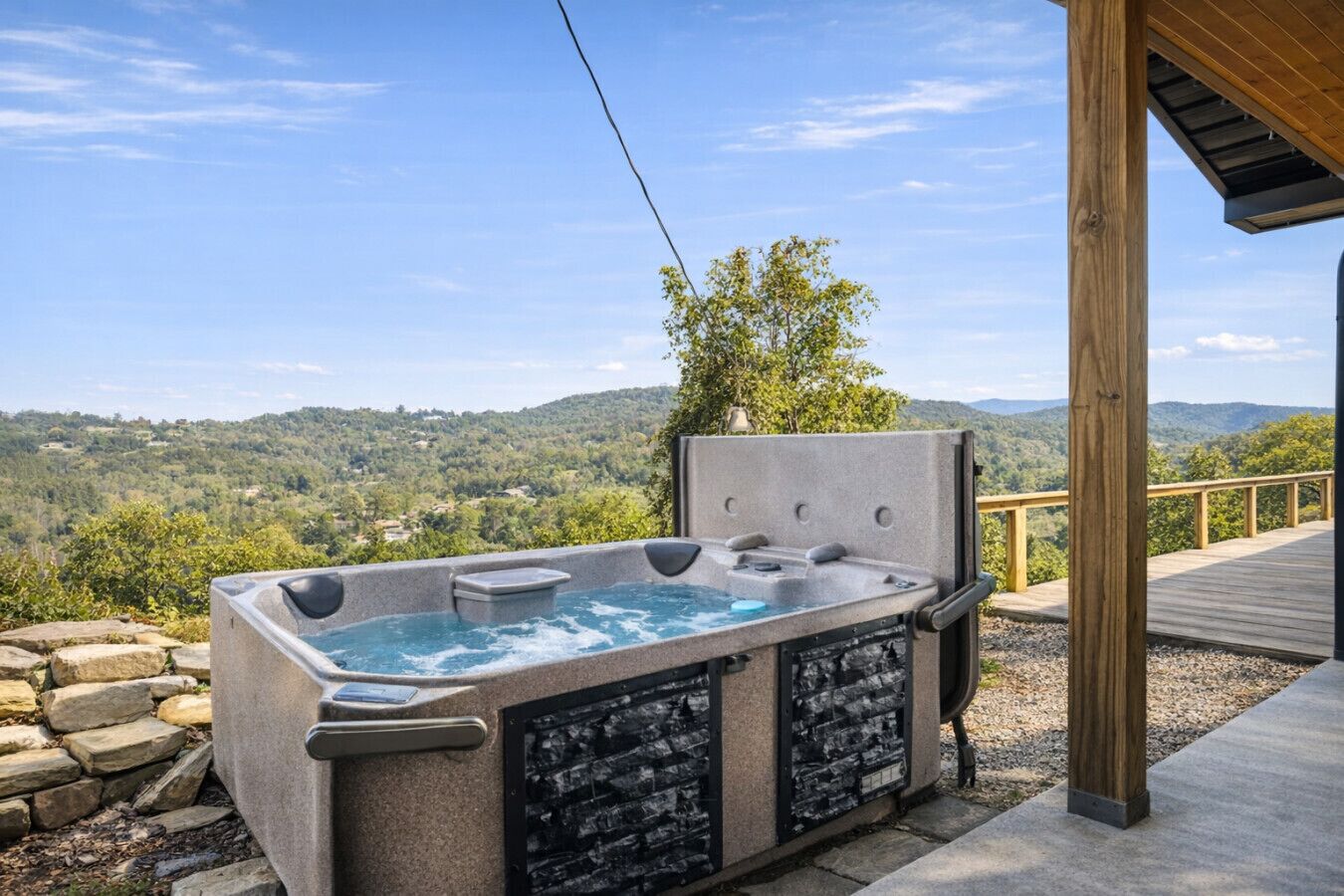 Een hottub met een stenen buitenkant, gelegen op een houten terras met uitzicht op een bebost landschap.
