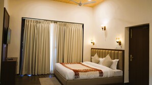 Ein Hotelzimmer mit Bett, Vorhängen, Deckenventilator, Wandleuchten und einer Holztür.