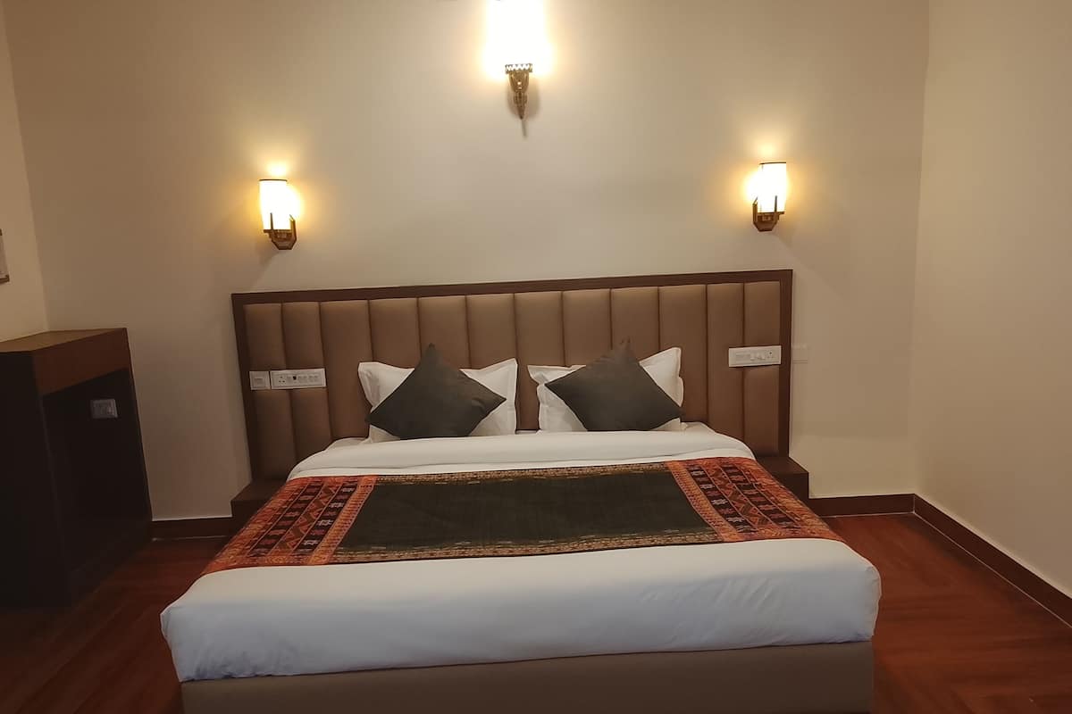 A neatly made bed with a headboard, two wall sconces, and a wooden floor.
