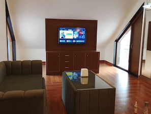Una sala de estar con un televisor de pantalla plana montado en la pared, un sofá, una mesa de centro y un ventanal corredero que da a un balcón.
