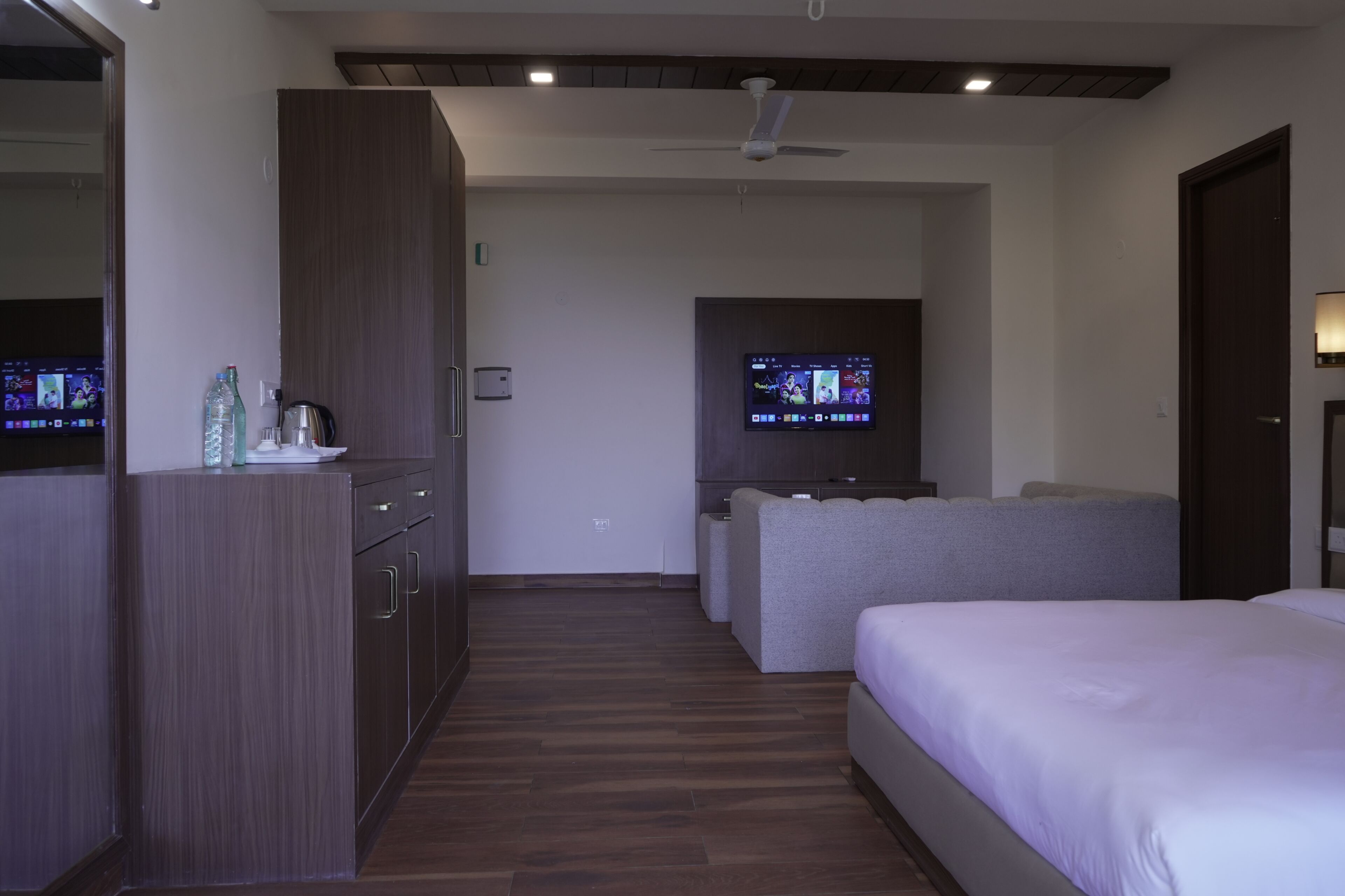 A modern hotel room with a wooden floor, a bed, a seating area, and a TV mounted on the wall.