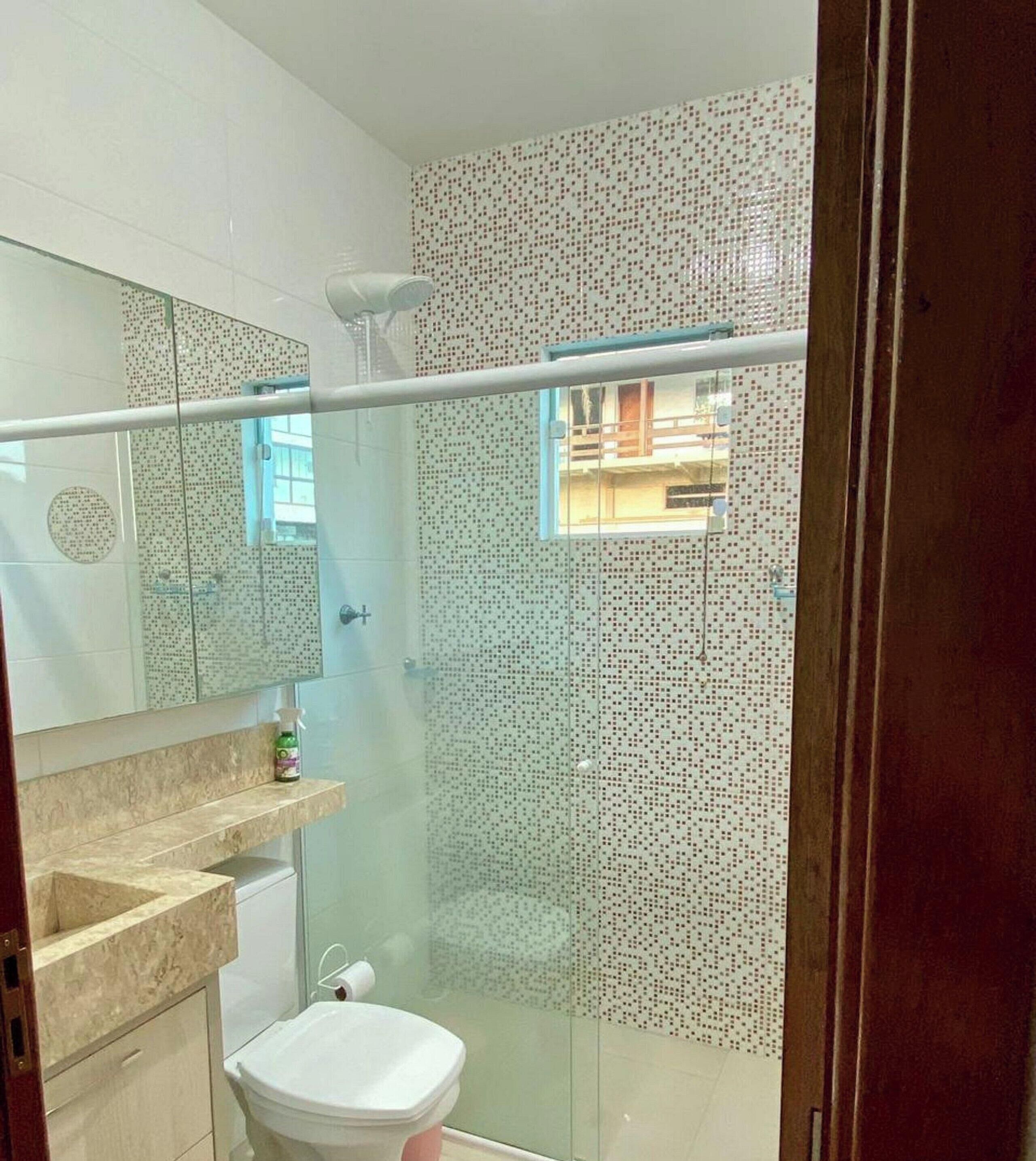 Une salle de bain avec une douche à parois de verre, des toilettes, un lavabo avec un miroir et un mur de douche décoré d'un motif.