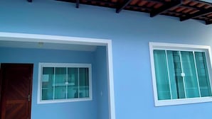 A building with a blue exterior, two windows with white frames, and a brown roof structure. - Casa Aconchego Barra Velha - SC (Barra Velha)
