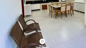 A modern kitchen with white cabinets, a black countertop, and a dining area with wooden chairs and a table. - Casa Aconchego Barra Velha - SC (Barra Velha)