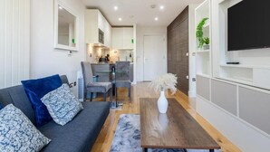 A modern living room with a sofa, coffee table, and a TV mounted on the wall. - Stunning Studio Flat Minutes From Lewisham Station With View (London)