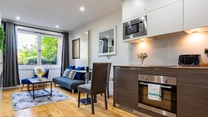 A modern kitchen with a built-in oven and microwave, a dining area with a table and chairs, and a large window with curtains. - Stunning Studio Flat Minutes From Lewisham Station With View (London)
