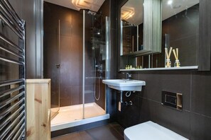 A modern bathroom with a glass-enclosed shower, a white sink, and dark tiled walls. - Stunning Studio Flat Minutes From Lewisham Station With View (London)