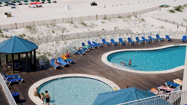 Un espace piscine comprenant deux piscines, des chaises longues et une plage en arrière-plan.