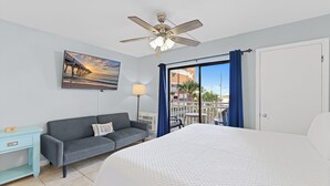 Une chambre d’hôtel avec un lit, un canapé, un bureau, un ventilateur de plafond, un tableau et une vue sur l’extérieur.