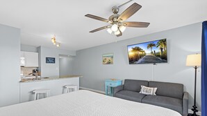 Une chambre d’hôtel équipée d’un lit, d’un ventilateur de plafond, d’un bureau, d’une kitchenette et offrant une vue sur la plage.