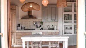 Une cuisine moderne avec une table blanche, des chaises transparentes, des luminaires suspendus en osier et un four encastré.