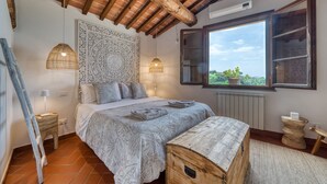 Une chambre à coucher avec un lit, des lampes de chevet, une fenêtre donnant sur un beau paysage, un plafond en bois et une tapisserie murale.