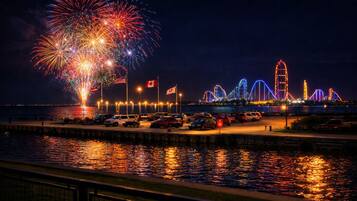 Vista para a orla marítima com fogos de artifício, montanha-russa e área de estacionamento.