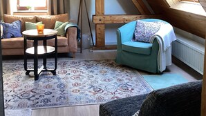 Una habitación acogedora con techo inclinado, un sofá, una silla, una mesita y una lámpara.