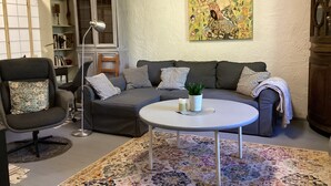 Una sala de estar con un sofá gris, una mesa redonda de centro, un tapete estampado, una estantería y un cuadro en la pared.