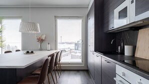 Una cocina moderna con una isla grande, armarios oscuros y vistas de la ciudad a través de amplios ventanales.