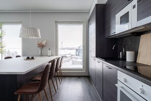 A modern kitchen with a large island, dark cabinetry, and a view of the city through large windows. - Luxurious Penthouse - Hot Tub & Sauna (Tampere)