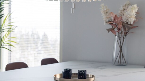 Un comedor moderno con una mesa de mármol blanco, una lámpara colgante decorativa y un jarrón con flores.