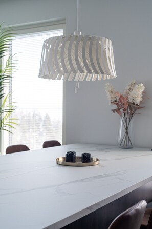 A modern dining area with a white marble table, a decorative hanging light fixture, and a vase with flowers. - Luxurious Penthouse - Hot Tub & Sauna (Tampere)